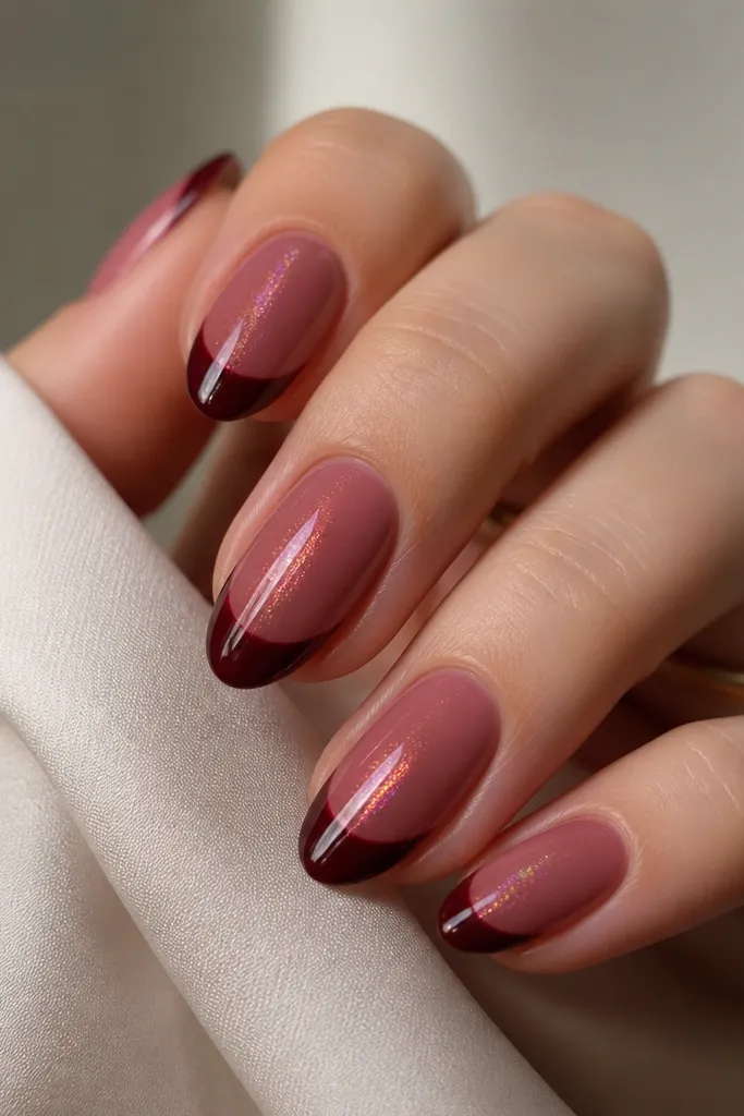 Short almond nails. The base is sheer rose. French tips are a glossy wine burgundy. A magnetic cat eye glow runs vertically through the nail center, reflecting red-purple highlights.