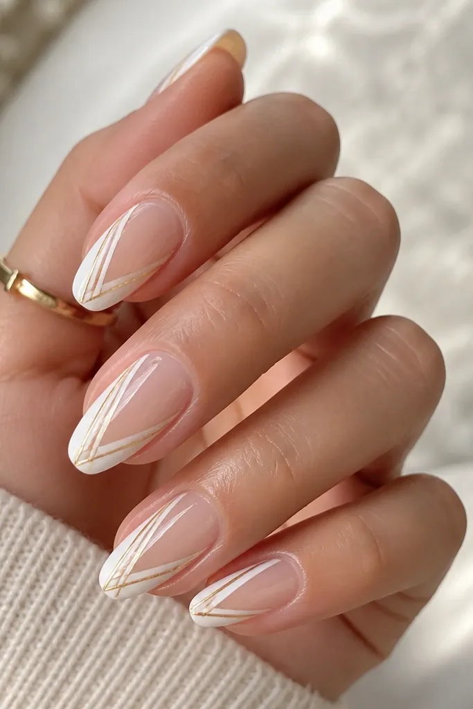 Nails have a glossy clear nude base with a clean white V-shape or diagonal negative space panel. Over the white panel are 2-3 micro gold stripes, each line thin and straight, with sharp edges.