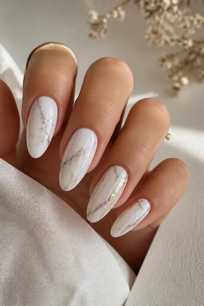 Long almond nails with a creamy white base and thin grayish marble veining. A few tiny gold leaf flecks sit near the sidewalls of two accent nails. The finish is glossy and smooth.