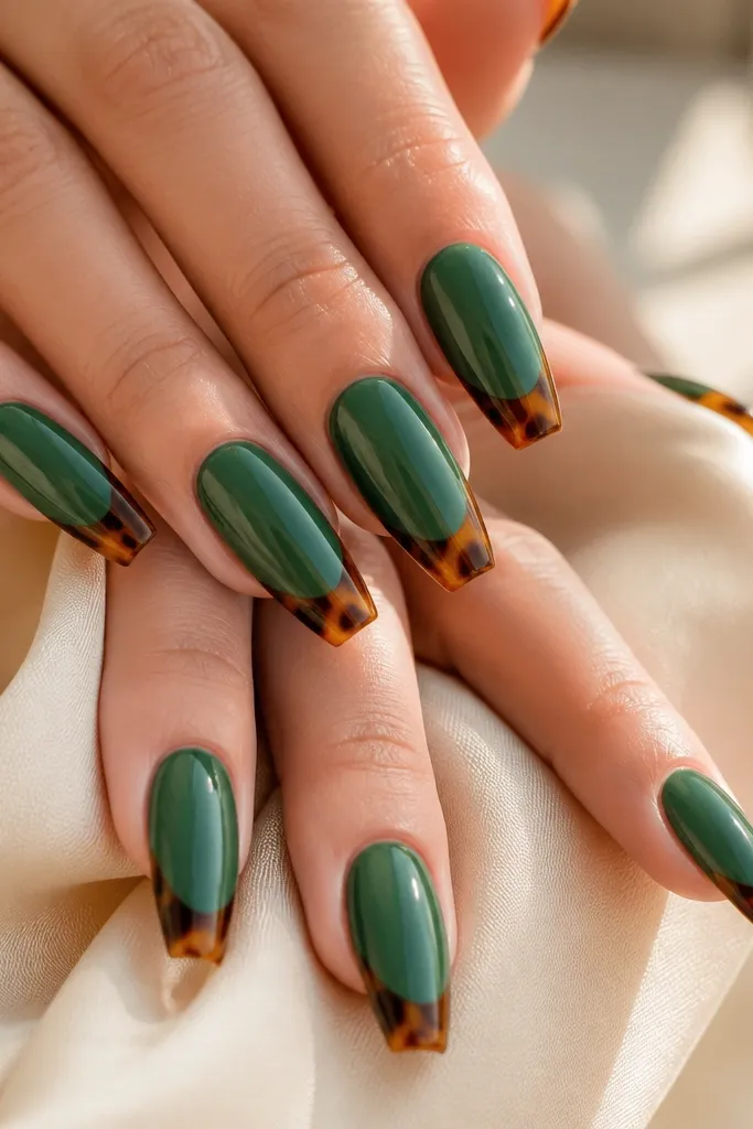 Medium coffin nails with a soft emerald green base. The tips have a crisp French shape, but instead of solid color, the tip area shows mottled tortoiseshell bands in caramel and dark brown. The cuticle line stays clean and the gloss is bright.