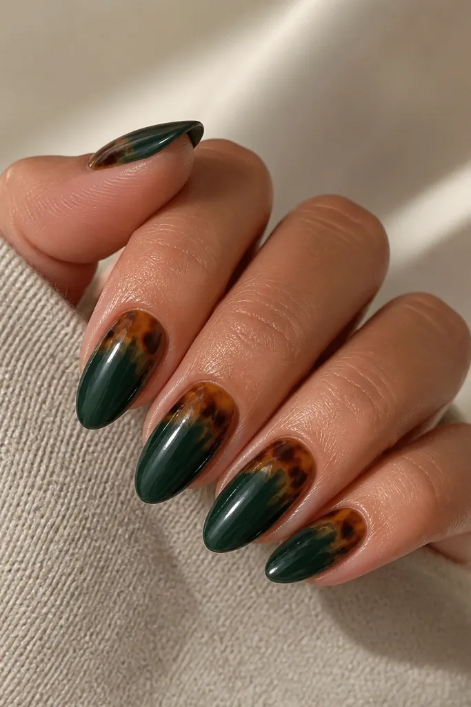 Medium almond nails with a deep green base. At the cuticle, a half-moon area shows tortoiseshell marbling in caramel and dark brown, fading outward into the green so the rest of the nail looks solid. Glossy finish with a clean cuticle edge.