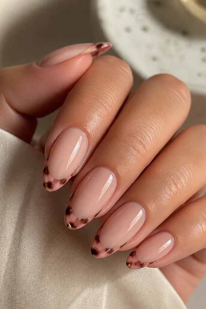 Medium almond nails. The cuticle area is bare-looking with a sheer nude base. French tips are painted in a blush-pink tortoise pattern with thin dark-brown lines and small honey highlights near the tip edge. The nails have a high-gloss shine and clean sidewalls.