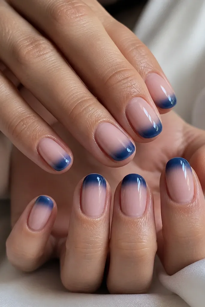 Short oval nails with a soft pink base and navy blue tips, blended like a gentle French fade, glossy.