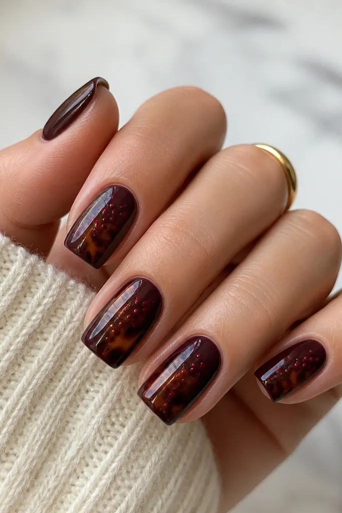Square nails in a plum-espresso base. Tortoise shell lines appear dark brown and caramel near the center. Tiny burgundy micro dots cluster along one side of each nail. Glossy.
