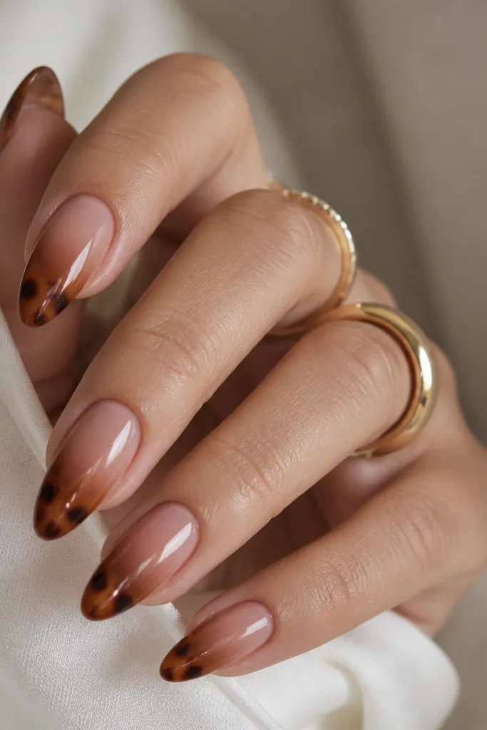 Almond nails with a sheer nude base that gradually turns warm brown near the tip. The topmost tip area has tortoise marbling with amber and dark brown. Glossy finish.