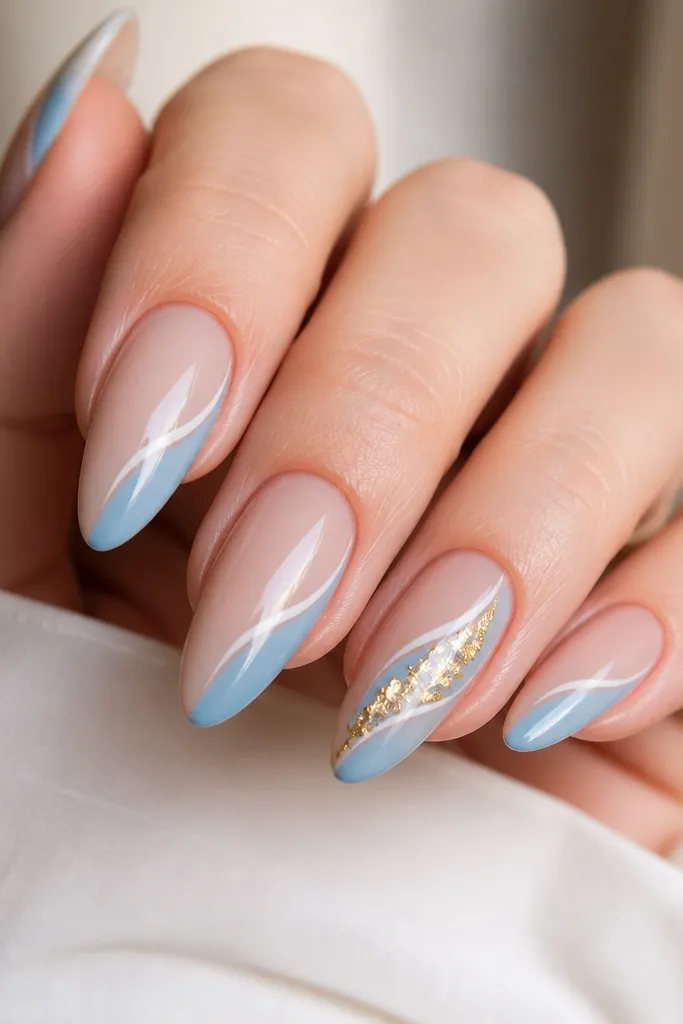 Almond nails with a glossy nude base. A diagonal blue-white panel runs from lower left near the sidewall to upper right near the tip. On one accent nail, gold foil chunks sit on the diagonal line like broken jewelry.
