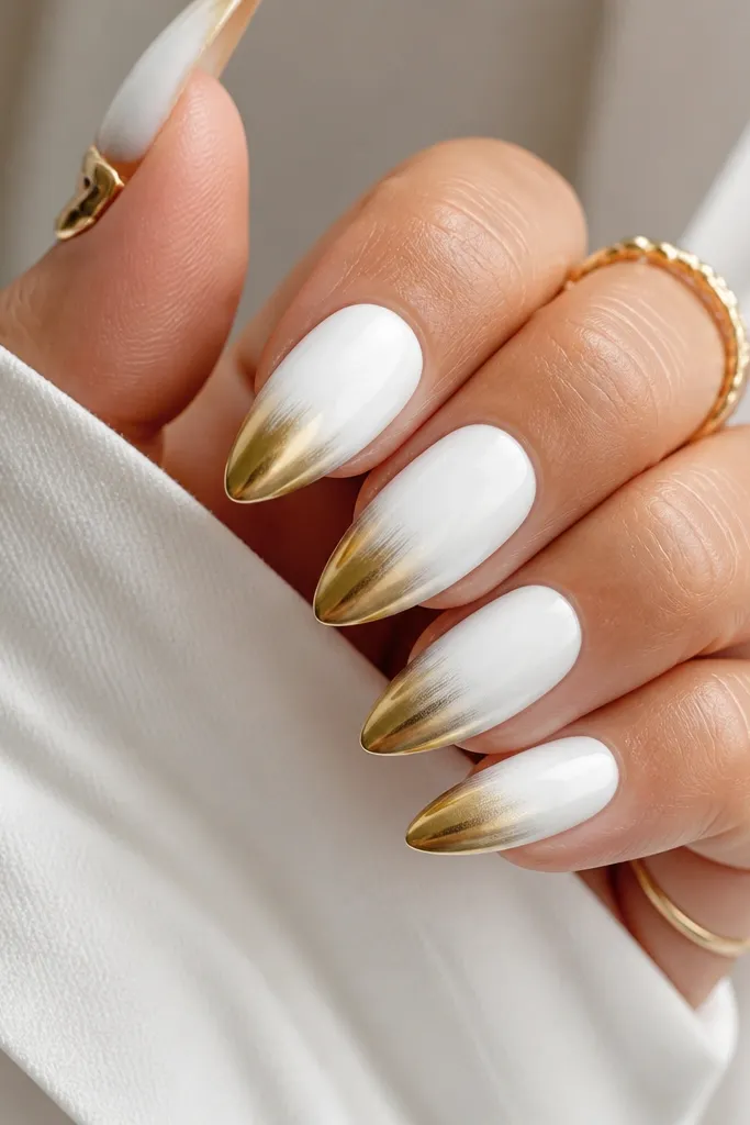Almond nails painted fully in opaque blue-white. The outer third of each nail is coated in gold chrome, creating a metallic gradient at the tip. The rest is glossy white with sharp edges.