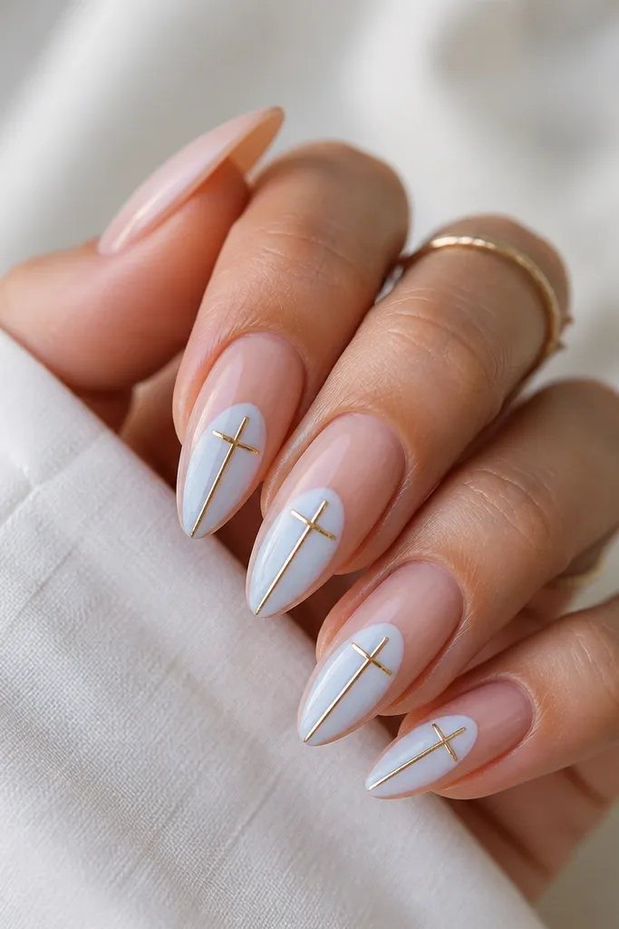 Almond nails with a nude base and a blue-white negative space shape. A thin gold cross sits in the center of the blue-white area, with one arm reaching toward the tip.
