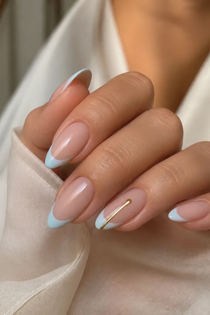 Almond nails with nude base. The tips are blue-white french. On the ring finger, a thin gold drip line starts from the french edge and tapers downward toward the center, glossy and metallic.