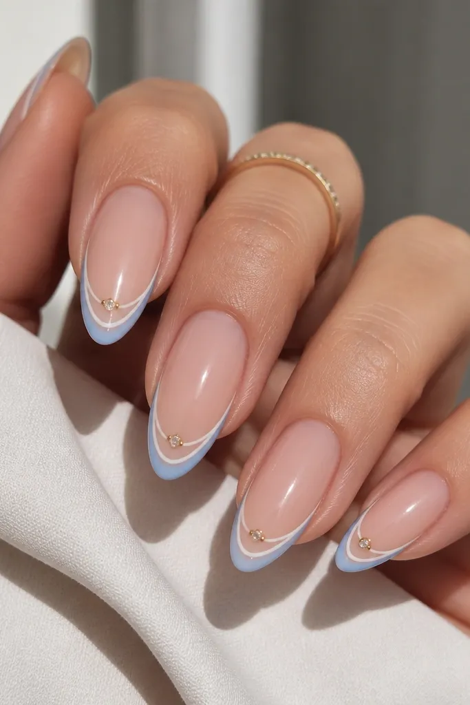 Almond nails with sheer nude base. A blue-white outline traces the french tip shape. At the outer corners of the tip, tiny gold-toned gem settings hold small clear stones.