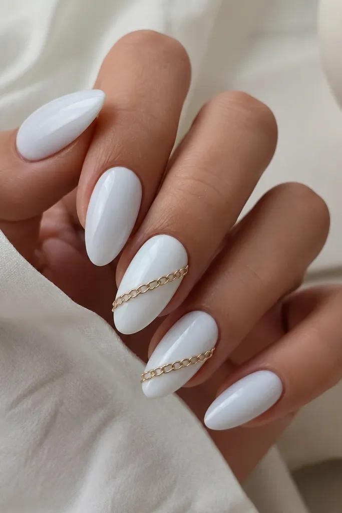 Almond nails painted solid glossy blue-white. A gold chain detail runs diagonally across the tip area on two accent nails, with small links catching light. The chain sits on top of the white and is sealed smooth.