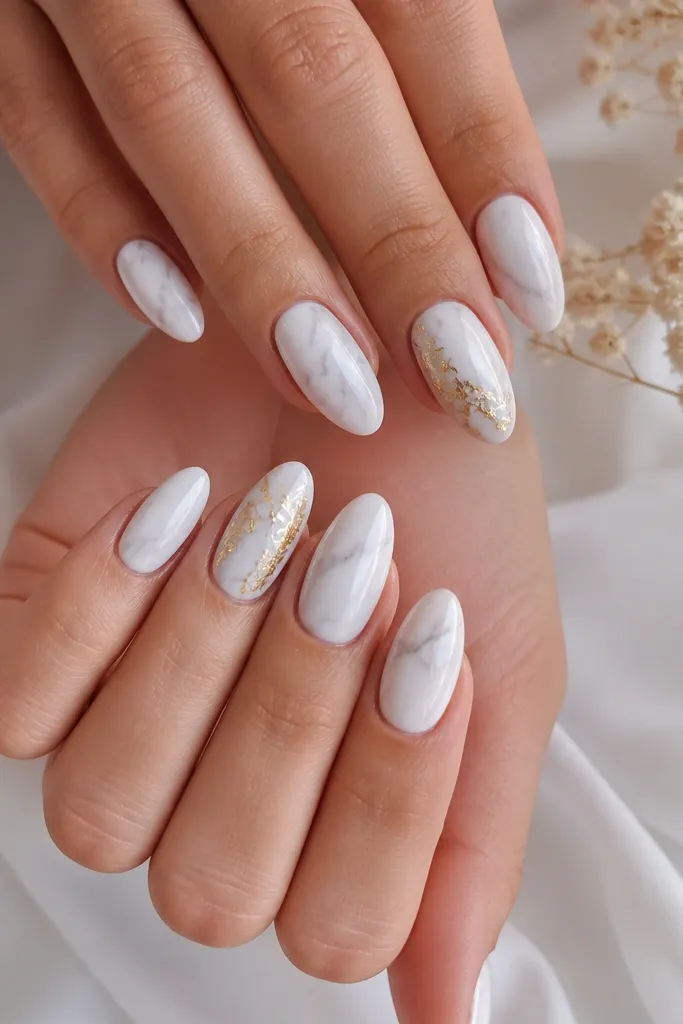 A medium almond set where most nails are milky white with soft greyish marble veining. One accent nail on each hand has torn gold leaf pressed into the marble, with irregular edges and a high-shine top coat. Everything is glossy and clean with no glitter chunks.