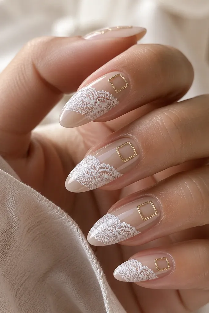 Almond nails with a sheer nude base and a white lace pattern across the center of each nail. In the top corner near the sidewall, there's a small gold frame like a tiny rectangular border. The lace is crisp and raised slightly under glossy top coat.