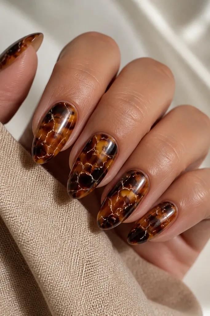 Almond nails with a warm tortoise base (golden caramel and dark brown). Thin white veins run through the shell like marbling, creating a "reverse" look. Nails are glossy and the veins are crisp, not cloudy.