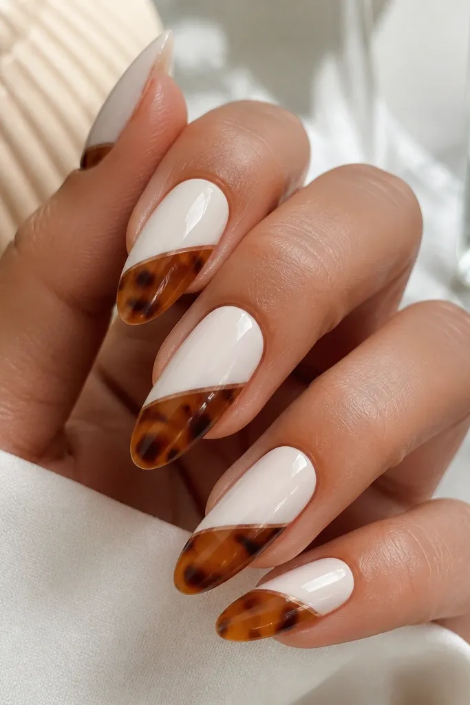 Long almond nails split diagonally into two halves. The lower half is tortoise in warm brown and caramel with tiny white breaks. The upper half is milky white with a very thin micro outline separating the sections. Glossy finish.