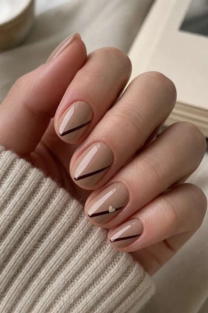 Short oval nails in mocha nude. On each nail, a single diagonal stripe runs from mid-side toward the tip in glossy black-brown. On one nail, a tiny heart in soft cream sits at the stripe's endpoint.