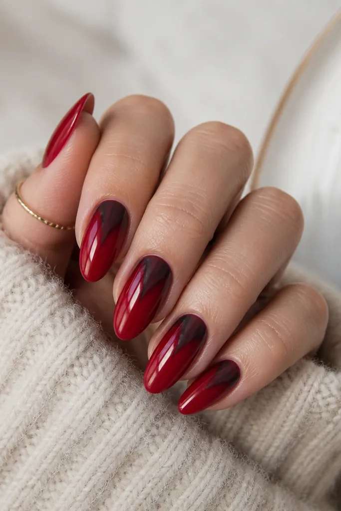 Almond nails in a rich red glossy finish. Near the cuticle, there's a smoky black V shape that points upward and is feathered at the edges. The V is centered on each nail, with the rest of the nail remaining solid red.