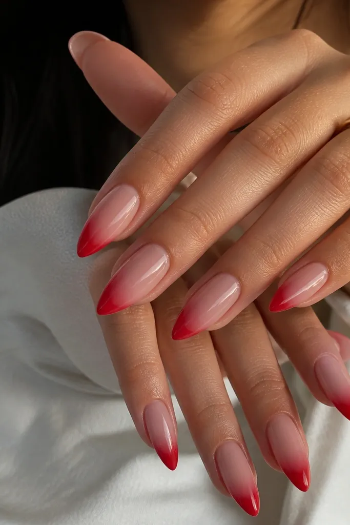 Almond nails with a nude base that transitions into red at the tips. The red is strongest at the outer edge and fades toward the smile line; the overall look is glossy and smooth.