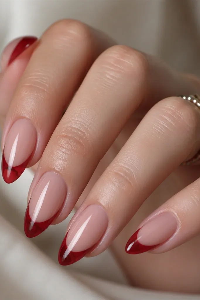 Almond nails with a nude base and red french tips that look translucent, like a glossy red glaze. The smile line is defined but the red has a jelly-like depth.