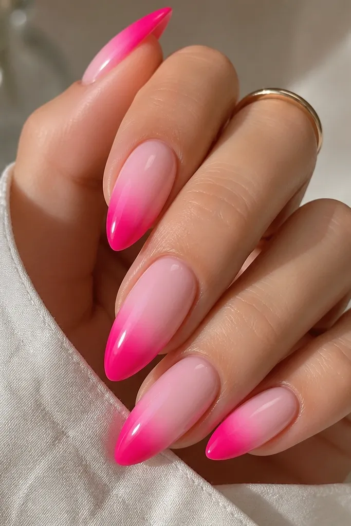Almond nails with a hot pink ombre that is strongest near the tip. The center of each nail fades into a pale white-pink glow, with smooth blending and a glossy finish.