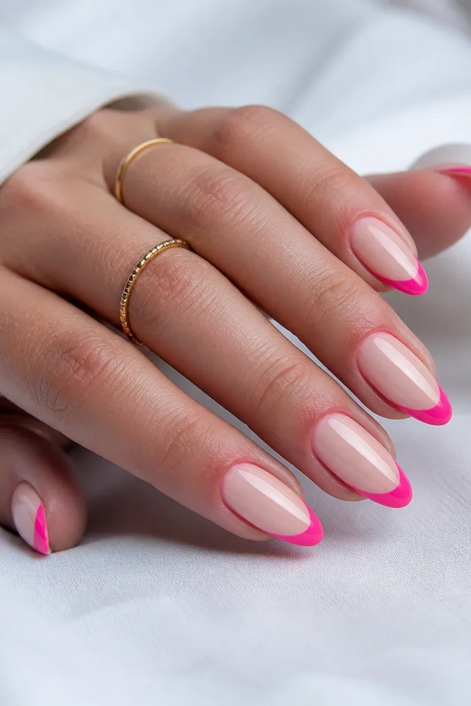 Almond nails with a sheer nude base. The tips are painted hot pink in a clean French shape, and the smile line stays clear and sharp, creating a crisp separation.