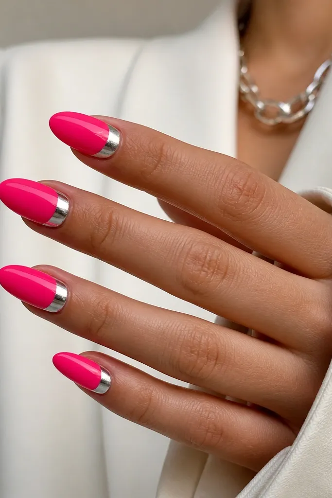 Almond nails painted hot pink with a silver chrome half-moon near the cuticle. The chrome is reflective and sharply defined, with a glossy top coat on the pink.