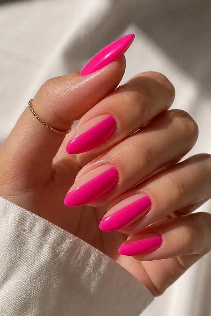 Almond nails in hot pink with a clean triangle of clear negative space on one side of each nail. The triangle is sharp, the pink is glossy, and the clear area shows the natural nail underneath.