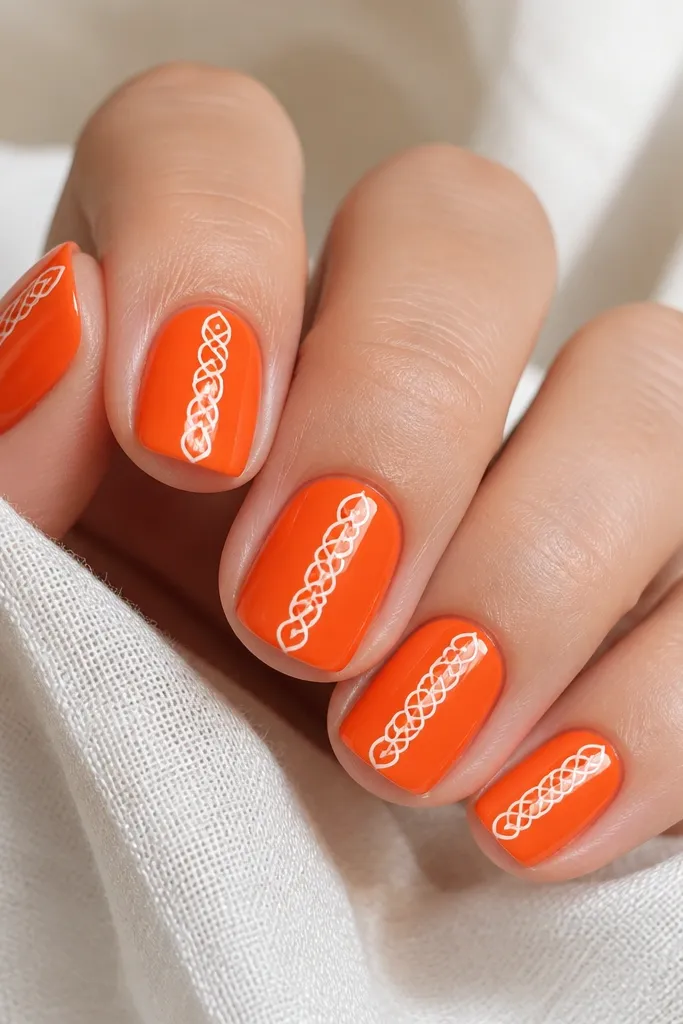 Short square nails in bright tangerine orange with a glossy finish. Each nail has a thin white striping pattern that looks like lace - small connected loops running down the center. The design is crisp and evenly spaced.