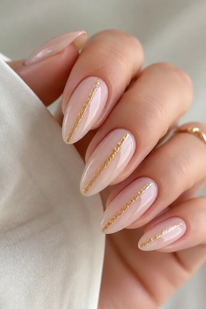 Almond nails in a milky pink base with a vertical gold foil strip running down the center. The foil looks slightly textured and reflective, like torn metal leaf. The strip is thin and crisp, and the rest of the nail is sheer and glossy.
