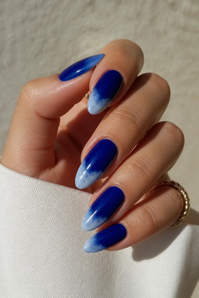 Almond nails with a deep royal blue base and soft, cloud-like white tips. The white is blended into the blue with a fuzzy edge, like small clouds at the end of each nail. The nails look glossy and smooth, with no hard line between colors.