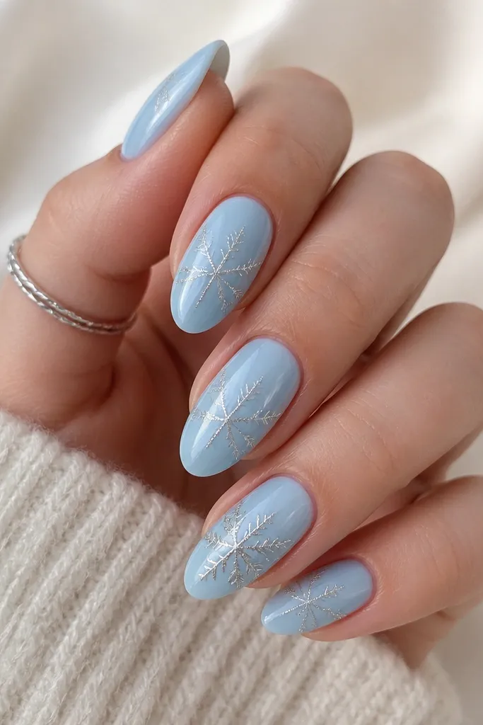 Medium almond nails in glossy ice blue. Thin silver lines form snowflake "veins" around the center, branching toward the tip on each nail. One thumb has a larger snowflake with denser lines, no chunky glitter.