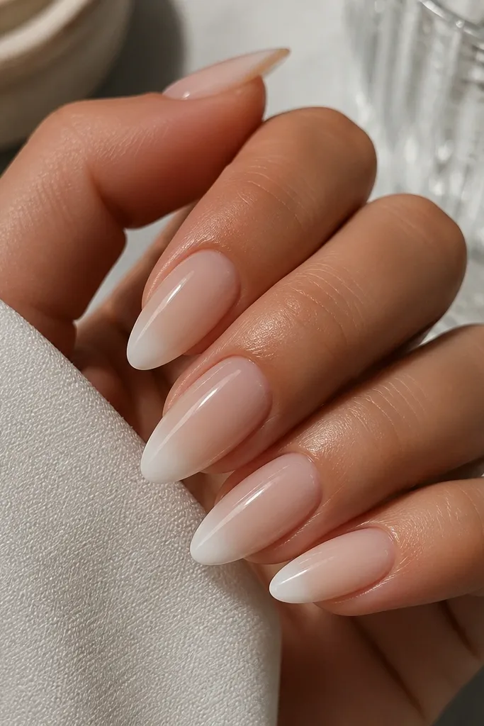 Medium almond nails with nude BIAB base that fades into a white French tip. The fade is smooth, with a crisp outer edge and no harsh banding. High gloss top coat.