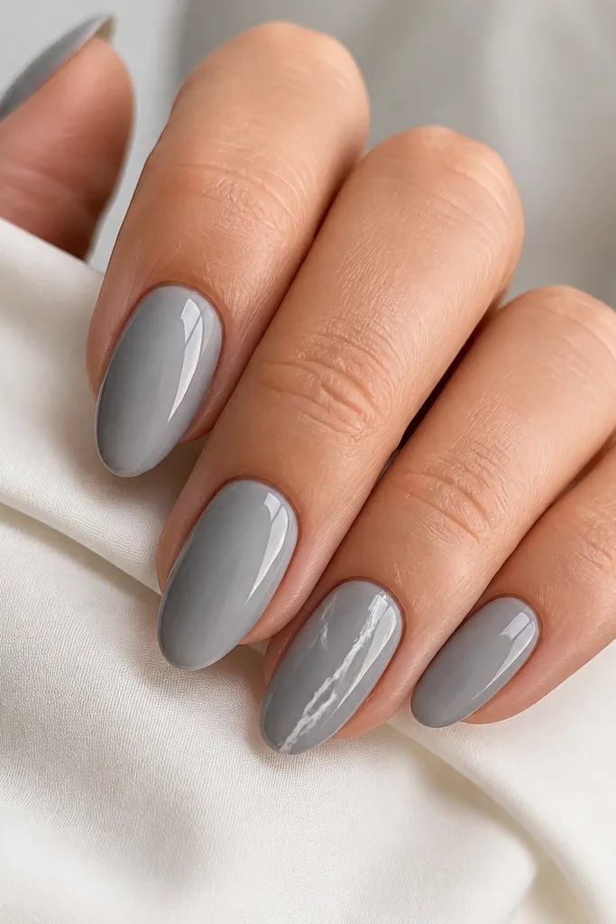Short almond nails in glossy light grey. The ring finger has a white marble vein that runs diagonally from near the cuticle to the tip, with small wispy branches. Other nails are plain grey.
