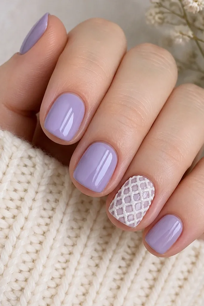 Short rounded nails in glossy lavender. One accent nail has a raised white lattice texture like crochet stitches, with small loops and a grid pattern. Other nails are smooth lavender.