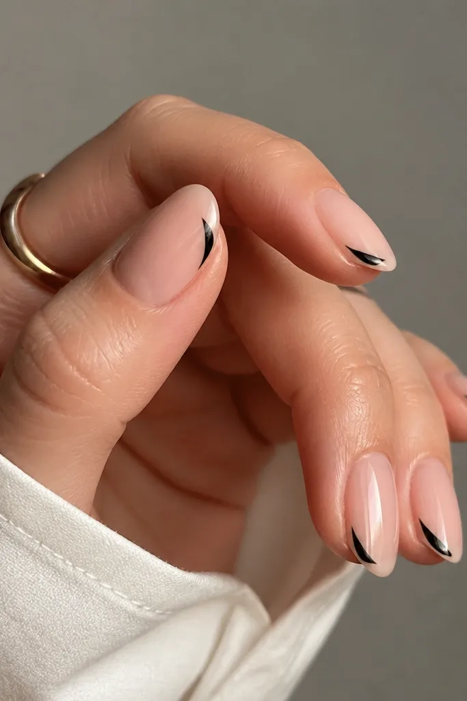 Short almond nails in nude BIAB. On each nail, there's a black wing shape on the outer tip corner, like a small eyeliner flick. Glossy topcoat.