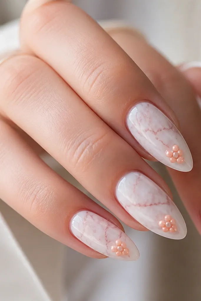 Almond nails have a milky white marble base with soft grey-pink veining. On each nail, there are small peach dot clusters near the lower center of the nail, like tiny grouped pearls. The finish is glossy and bright.