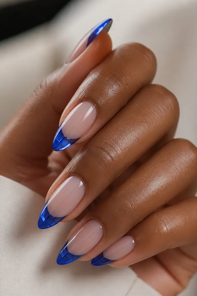 Medium almond nails with a sheer nude base, cobalt blue tips that look like stained glass, and a thick clear gel overlay that creates a glossy, glassy dome.