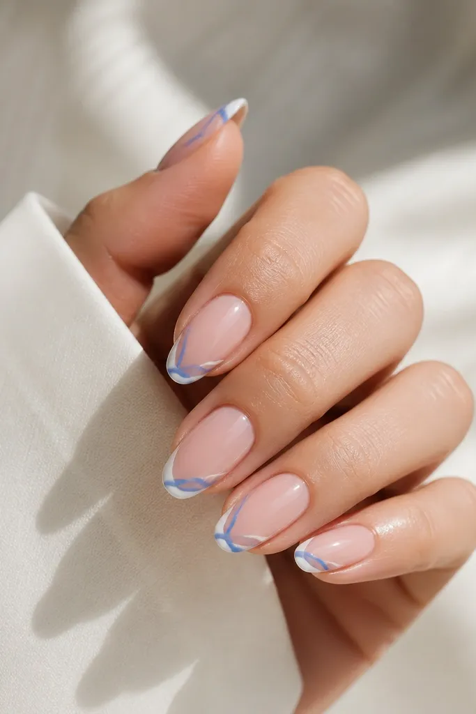 Medium almond nails with a sheer pink base and cornflower blue ribbon-like lines wrapping the tip edges; the tips have a thin white border.