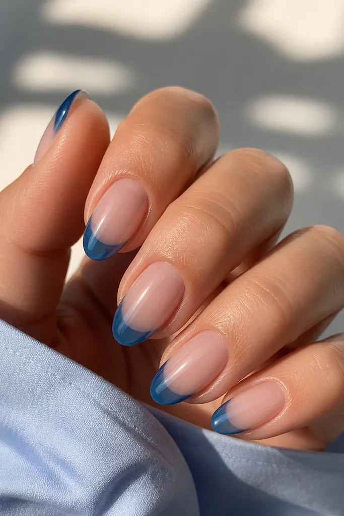 Short almond nails with a nude base and translucent blueberry-blue jelly tips; light shows through the gel like a candy layer.