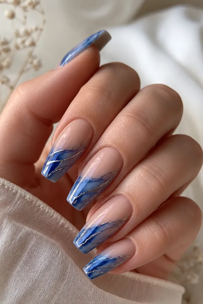 Medium coffin nails with indigo blue marble swirls on a nude base; thin silver lines run through the marble like veins.