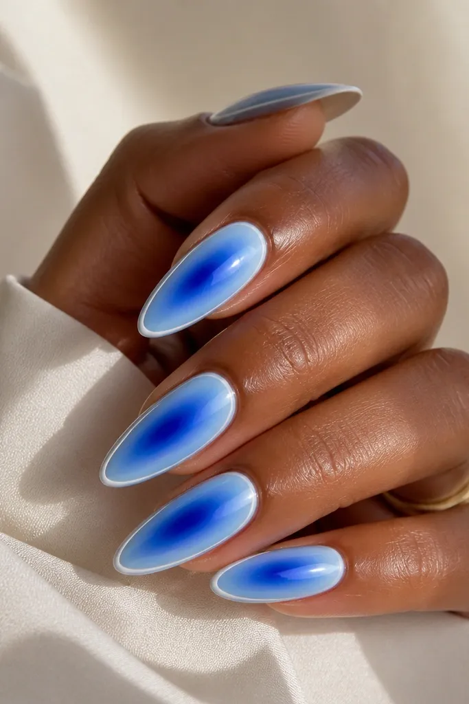 Long almond nails with a cobalt-to-icy blue gradient radiating from the center; a thin white outline frames the gradient on each nail.