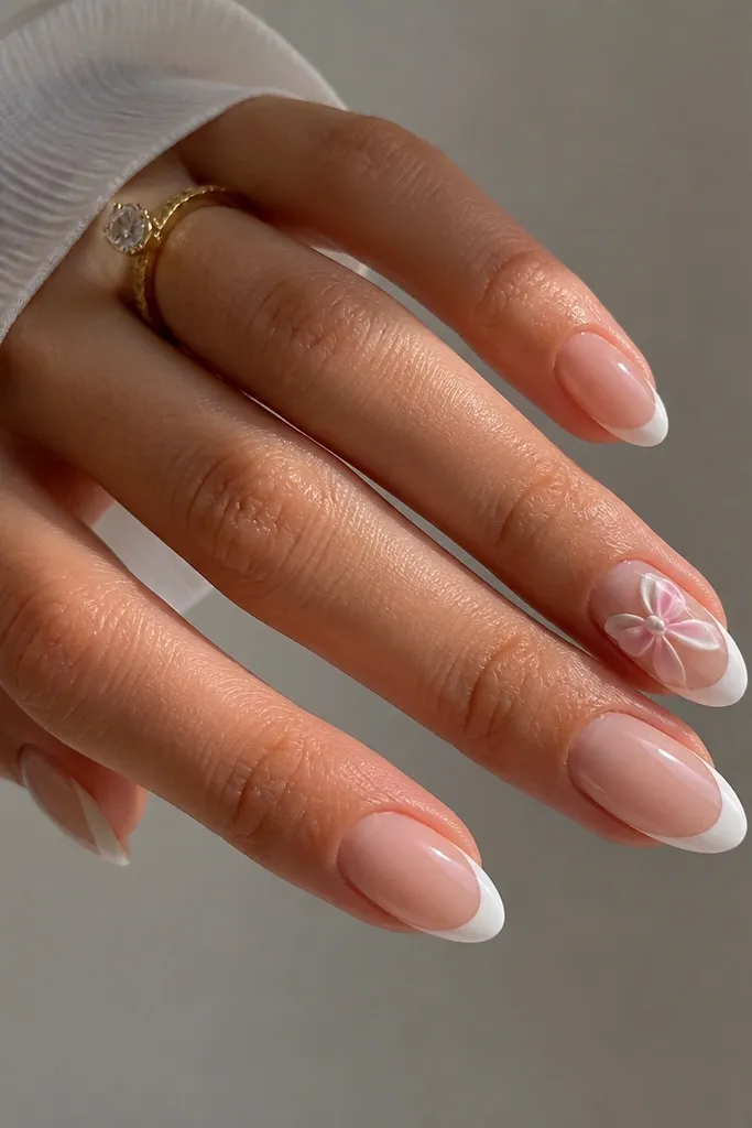 Short almond extensions with a milky white French tip. The nude base is sheer and glossy. On the ring finger, there is a small 3D bow painted in pale pink and white with a tiny dot center. Other nails have only the French.