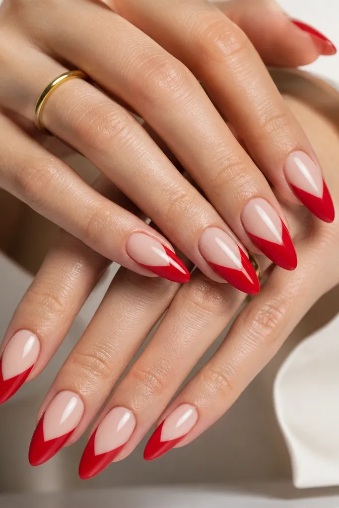 Almond nails where the tips are bright red, but the base has a nude sheer window shaped like a clean V starting near the center of each nail. The V is sharp and symmetrical, and the red tip has a smooth curve.