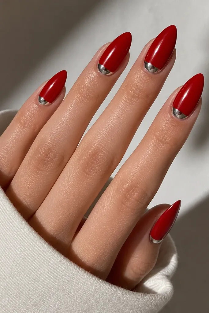 Almond nails in bright red with a silver chrome half-moon at the base of each nail. The chrome is reflective and sits cleanly under the cuticle, forming a curved crescent that looks metallic.