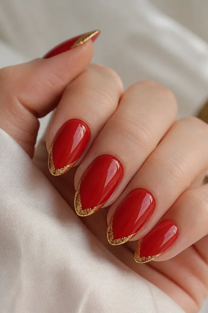 Almond nails with bright red base and a classic french tip line. The french line is covered in thin gold foil that looks torn and metallic, with a glossy topcoat over everything.