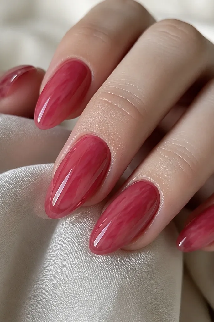 Almond nails with a translucent cherry jelly pink-red base; faint red streaks run diagonally under a glassy topcoat.