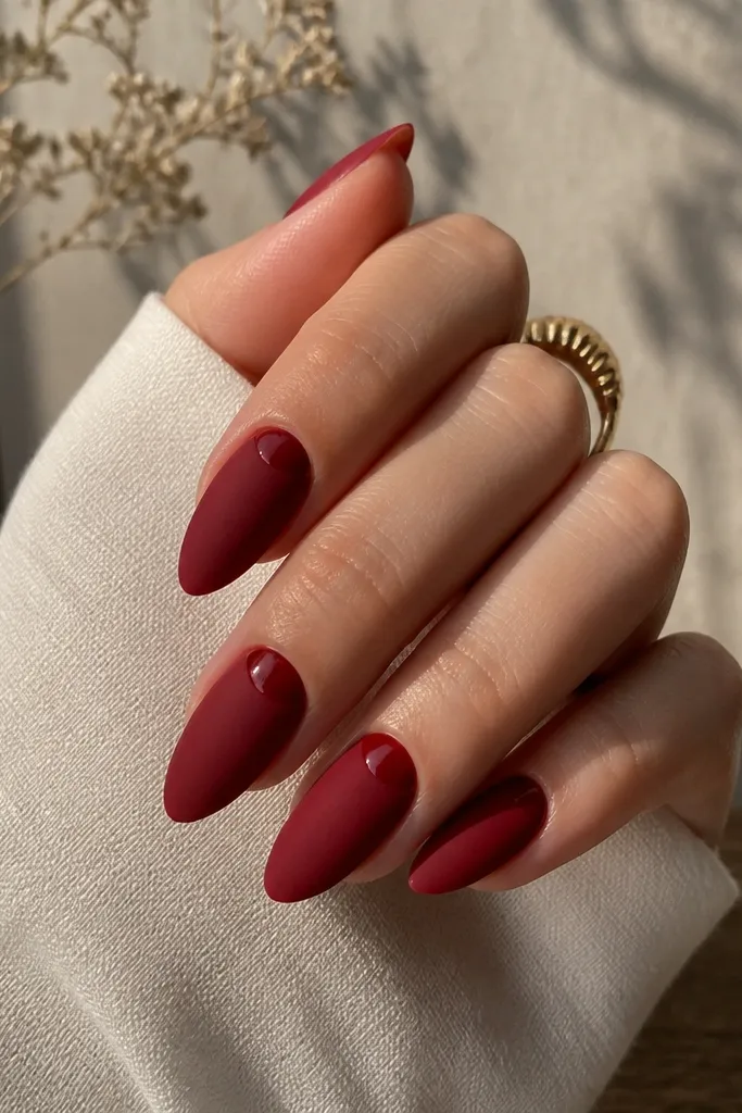 Almond nails in matte cherry red; a glossy half-moon near the cuticle is left shiny, creating a clean contrast band.
