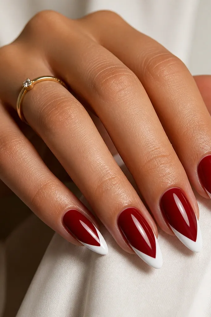 Almond nails with cherry red base and crisp white diagonal V-shaped tips pointing toward the center; glossy finish.