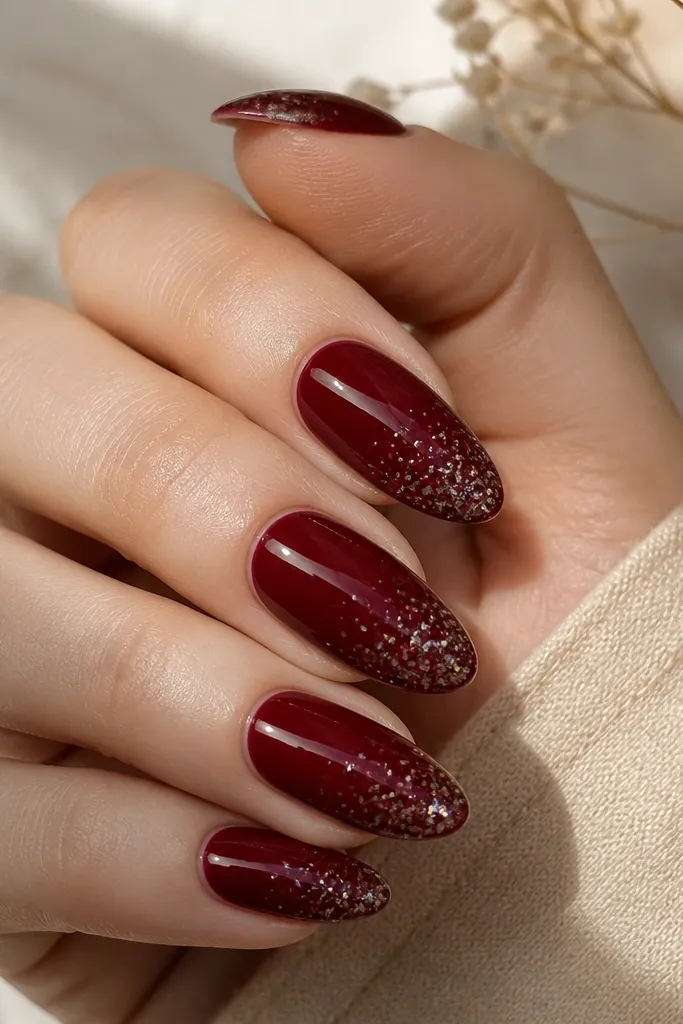 Cherry red almond nails with tiny holographic flakes concentrated near the tip; glossy topcoat creates a smooth glass layer.