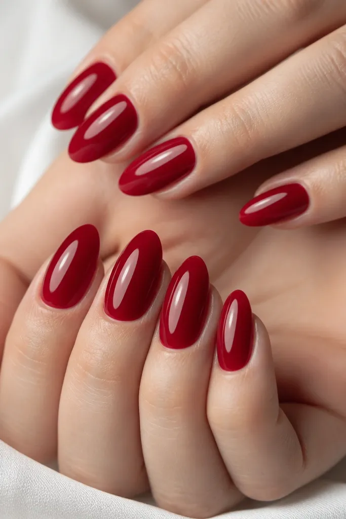 Ten nails in a uniform almond shape, glossy cherry red on all nails, smooth cuticles with a clean natural nail line, light reflections streaking across each nail like glass.